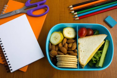 Okul öğle yemeği kutusu, kalem ve defter masanın üzerinde. Üstten görünüm.