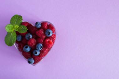 Ahududu ve yaban mersini menekşe arka plan üzerinde kalp şeklinde. Üstten görünüm. Kopya alanı.