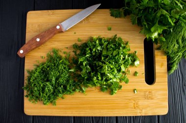 Kıyılmış maydanoz ve dereotu siyah ahşap arka plan üzerinde kesme tahtası üzerinde. Üstten görünüm.