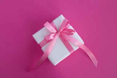 Koyu pembe arka plan üzerinde pembe Fiyonklu hediye paketi. Üstten görünüm. Kopya alanı.