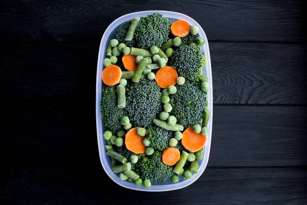 Frozen vegetables in the box on the black wooden background.Top view.Copy space.Healthy food ingredients.