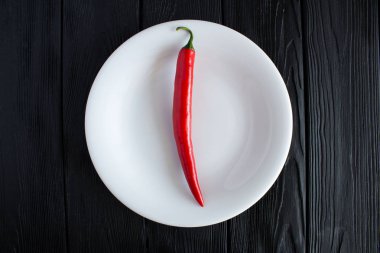 One pepper chile  on the white plate on the black wooden background.Top view.Diet minimal concept.