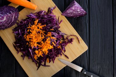 Kıyılmış taze mavi lahana ve havuç siyah ahşap zemin üzerine kahverengi kesme tahtası üzerinde. Üstten Görünüm. Kopya alanı.