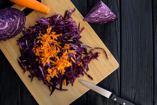 Свежая голубая капуста и морковь на коричневой разделочной доске на черном деревянном фоне.
.