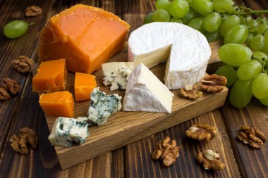 Peynirler, üzüm ve fındık kahverengi ahşap zemin üzerinde