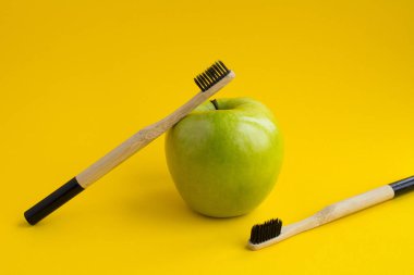 İki bambu diş fırçası ve Sarı zemin üzerine yeşil elma. Kopya alanı.