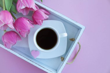 Siyah kahve Kupası ve Pembe Lale pembe arka plan üzerinde beyaz ahşap tepsi içinde. Üstten Görünüm. Portre.