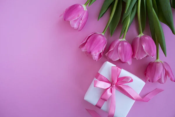 Gift with pink bow and pink tulips on the pink background.Top view.Copy space.