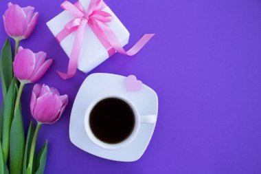 Siyah kahve beyaz Kupası, pembe fiyonk ve mor zemin üzerine Pembe Lale ile hediye. Üstten Görünüm. Portre.