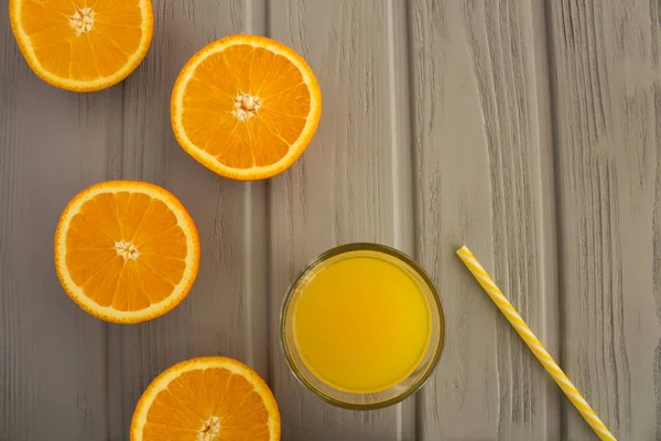 Orange juice in the glass  and halves of oranges on the grey wooden background.Top view.Copy space.