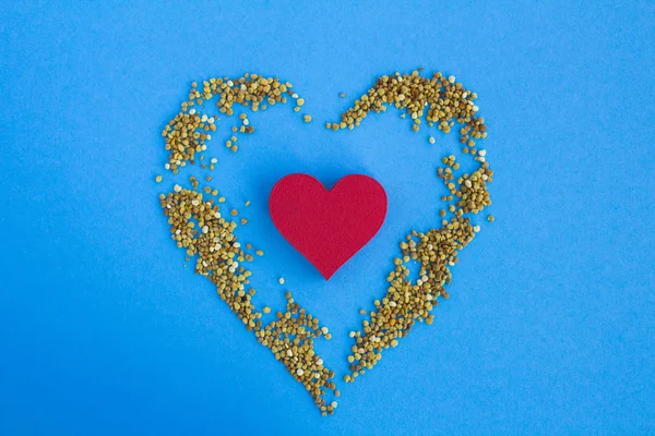 Red heart  and  bee pollen on the blue  background.Top view.Copy space.