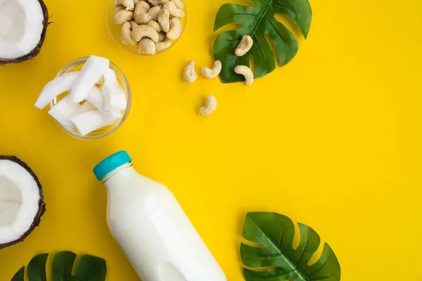 Coconut  milk in the glass bottle and cashew nuts on the yellow background.Top view.Copy space.
