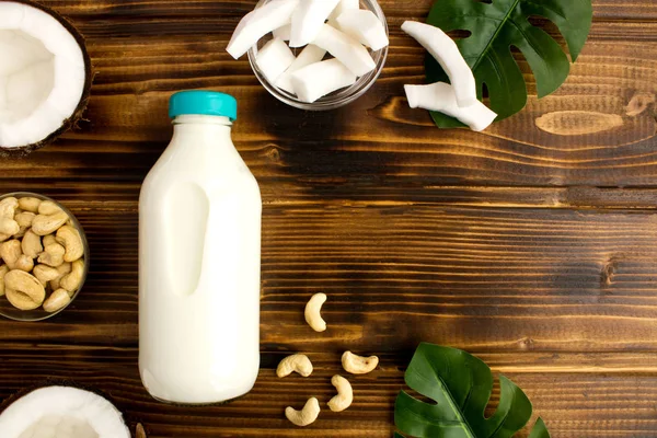 Coconut  milk in the glass bottle and cashew nuts on the brown wooden background.Top view.Copy space.
