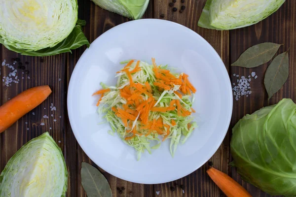 Salad with cabbage and carrot in the white plate on the brown wooden background.Healthy food ingredients.Top view.Copy space.