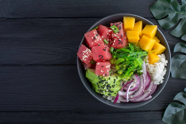 Poke bowl with tuna in the dark bowl on tropical the background.Top view.Copy space.