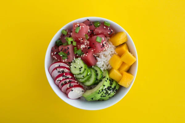 Poke bowl with tuna in the white bowl in the center of the yellow background.Top view.Closeup.