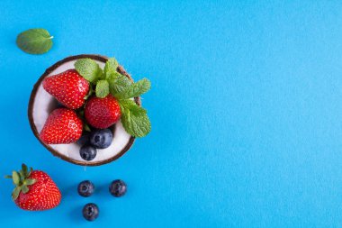 Mavi arka planda Hindistan cevizi, çilek ve yaban mersini. Üst görünüm.