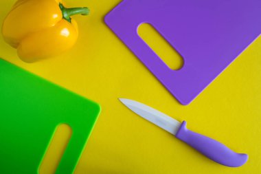 Sarı arka planda renkli kesme panoları, bıçak ve biber. Üst görünüm.