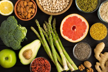 Superfood veya vejetaryen gıda konsepti. Siyah ahşap arka planda sebze, meyve, bakliyat, fındık ve arı polen. Üst görünüm.