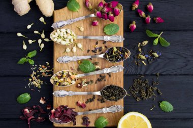 Çay kompozisyonu. Siyah ahşap arka plan üzerinde kahverengi kesme tahtası üzerinde gümüş kaşık çay farklı çeşitleri. Üstte görüntü.