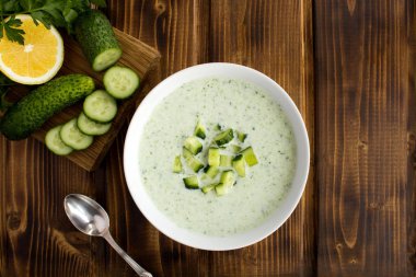 Kahverengi ahşap arka plandaki beyaz kasede salatalıklı yoğurt içecekleri..
