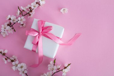 Pembe arka plan üzerinde pembe yay ve çiçekli ağaç dalları ile Hediye. Üst te. Kopyalama alanı.