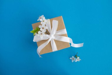 Mavi arka planda beyaz yay ve çiçekli ağaç dalları ile hediye. Üst te. Kopyalama alanı.