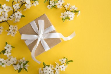 Sarı arka plan üzerinde beyaz yay ve çiçekli ağaç dalları ile Hediye. Üst te. Kopyalama alanı.