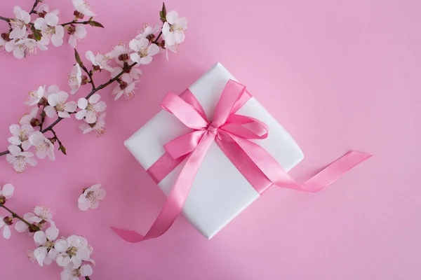 Gift with pink bow and flowering tree branches on the pink background.Top view.Copy space.