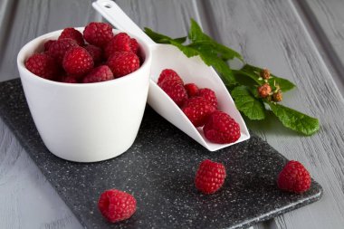 Beyaz plaka ve gri kesme tahtası üzerinde kepçe ahududu