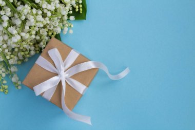 Mavi arka plan üzerinde beyaz kurdele ve vadinin zambaklar ile Hediye kutusu. Üst te. Kopya alanı. Closeup.