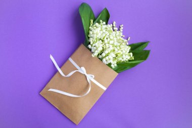 Leylak arka planda beyaz bir kurdele ile bağlı bir zarf içinde vadinin zambaklar. Üst te. Kopya alanı. Bahar çiçekleri kavramı.