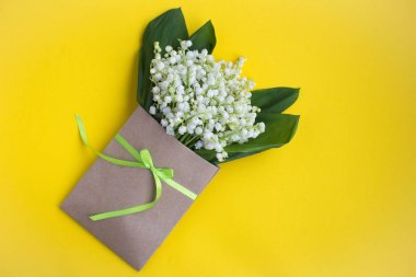 Sarı arka plan üzerinde yeşil bir kurdele ile bağlı bir zarf içinde vadinin zambaklar. Üst te. Kopya alanı. Bahar çiçekleri kavramı.