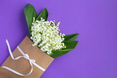 Leylak arka planda beyaz bir kurdele ile bağlı bir zarf içinde vadinin zambaklar. Üst te. Kopya alanı. Bahar çiçekleri kavramı.