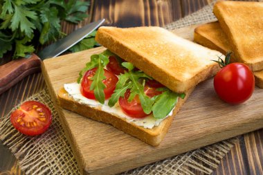 Ahşap kesme tahtası üzerinde domates ve arugula ile Vejetaryen sandviç