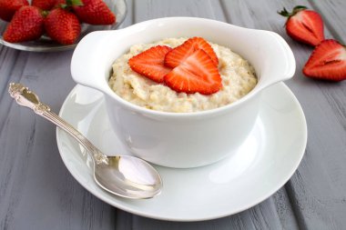 Gri ahşap arka plan üzerinde beyaz tabakta çilek ile yulaf ezmesi