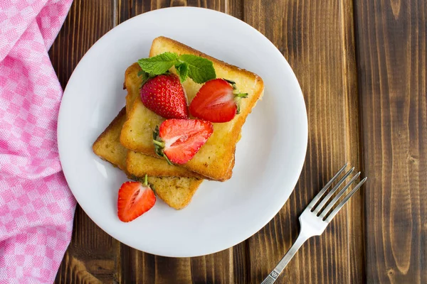 French toasts with  strawberries in the white  plate on the brown wooden background.Top view.Copy space.Closeup.