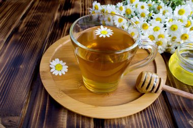 Kahverengi ahşap arka plan üzerinde papatya ve bal ile cam bardak Çay