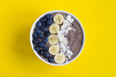 Sarı arka planda yaban mersini, muz ve hindistan cevizi cipsi ile Smoothies kase. Üst te. Kopyalama alanı.