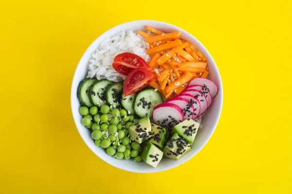 Vegan poke bowl with white rice and vegetables in the white  bowl in the center of the yellow background.Top view.Closeup.