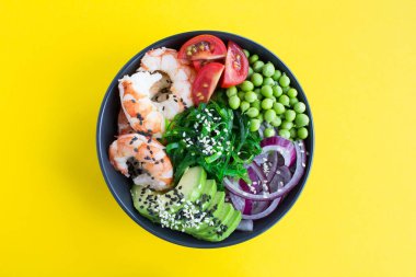 Sarı arka plan merkezinde karanlık kase kırmızı karidesler ve sebzeler ile poke kase. Üst görünüm. Closeup.