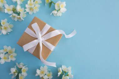 Mavi arka planda beyaz yay ve Yasemin çiçekleri ile hediye. Üst görünüm. Boşluk Kopyala.