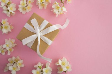 Pembe arka planda beyaz yay ve Yasemin çiçekleri ile hediye. Üst görünüm. Boşluk Kopyala.