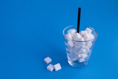 Mavi arka planda şeker küpleri ile Cam. Kopya alanı. Sağlıksız gıda konsepti.