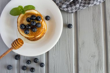 Gri ahşap arka plan üzerinde beyaz tabakta yaban mersini ve bal ile Krep. Üstte görüntü.