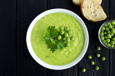 Siyah ahşap arka plan üzerinde beyaz kase içinde bezelye çorbası. Üstte görüntü.