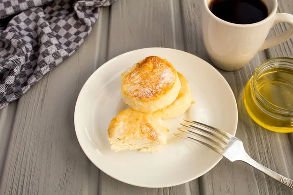 Breakfast: cheese pancakes, coffee  and honey  on the grey wooden background