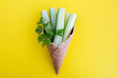 Sarı arka planın ortasında dilimlenmiş salatalık ve maydanoz ile dondurma konisi. Üst te. Kopyalama alanı.