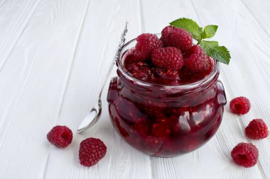 Beyaz ahşap arka plandaki cam kavanozda ahududu reçeli. Yakın çekim..