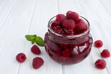 Beyaz ahşap arka plandaki cam kavanozda ahududu reçeli. Yakın çekim..